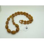 A Long Graduated Single Strand Mottled Amber Coloured Bead Necklace.