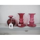 A Teign Valley Cranberry Glass Vase, together with a pair of similar candlesticks. (3)
