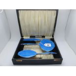 An Enamel Backed Three Piece Dressing Table Set, highlighted in blue, with a comb in original fitted