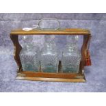 A Tantalus Circa 1920's, with glass spirit decanters, house in oak stand having plated mounts,