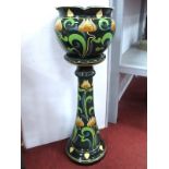 An Early XX Century Pottery Jardiniére and Stand, the dark green grounds painted in the Art