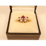 An 18ct gold diamond and ruby cluster ring, the large central ruby beset with six smaller rubies and