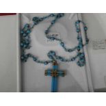 A turquoise and yellow metal cross on a matching 48 inch chain