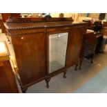 A 1930's mahogany display cabinet with glazed central door flanked by enclosed cabinets on short