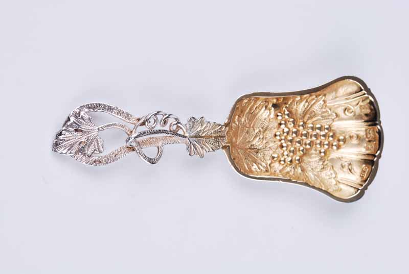 A modern silver caddy spoon with trailing vine tendril handle and grape and vine decorated bowl,