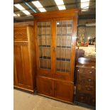 An Arts & Crafts oak elevated two door glazed bookcase with a pair of integral drawers on a two door