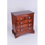An early 20th century mahogany minature chest of two over three drawers, with glass handles and on