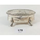 A silver oval trinket box with embossed landscape and figure decoration all on paw feet, Chester