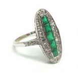 An 18 carat white gold Art Deco style ring set line of five emeralds within long oval diamond