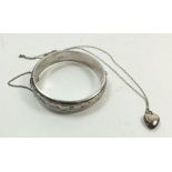 A silver engraved bangle and a silver small heart form locket on chain