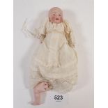A small jointed bisque baby doll with painted face, silk and lace gown, petticoat and knickers, 12cm