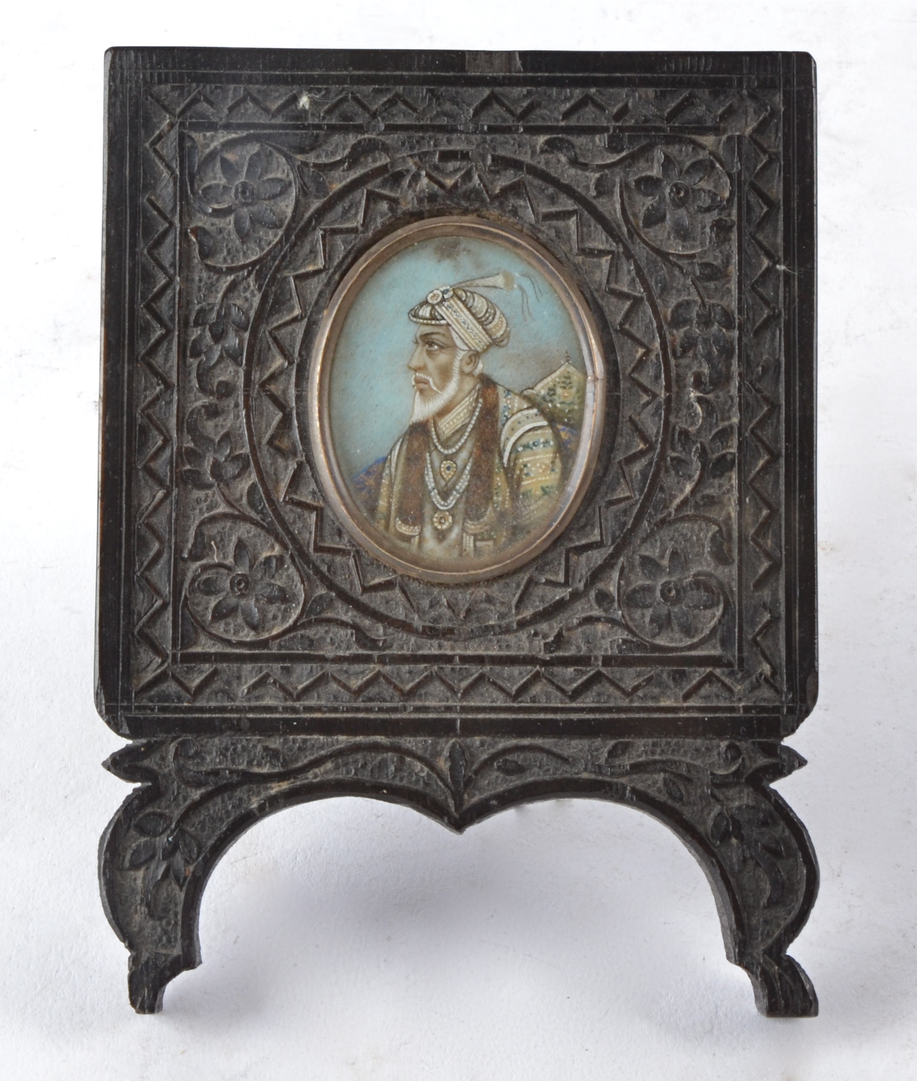 An oval Indian miniature portrait painting, encased in a profusely carved ebonised surround, 11cm