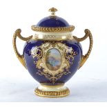 A late 19th Century Coalport twin handled urn and cover, with cartouches of lakeside landscapes, the