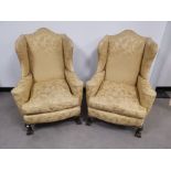 A pair of upholstered wing back arm chairs, set on claw and ball feet to the front. Floor to cushion