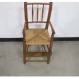 A vintage beech tall child's chair, spindle back, rush seat, round turned arms and supports, width