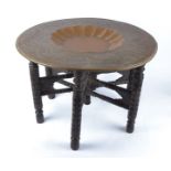 An Eastern embossed copper circular tray top table, raised on a six carved wooden legs, diameter