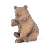 A Black Forest carved model of a seated bear, with one paw raised and black glass eyes, height