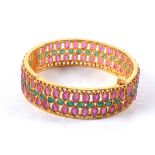 A decorative gilt bangle with semi precious red and green stones in the manner of rubies and