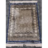 A Middle Eastern cream ground silk rug, with a blue border and repeating diamond pattern, tassels to