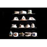 A large collection of crested china hats and helmets, including Tommy's Steel Helmet, Pith helmet,