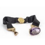 A George V amethyst and 9ct gold fob and silk ribbon, oval mixed cut amethyst on a pierced tapered