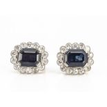 A pair of sapphire and diamond cluster ear studs, the emerald cut dark blue sapphires surrounded