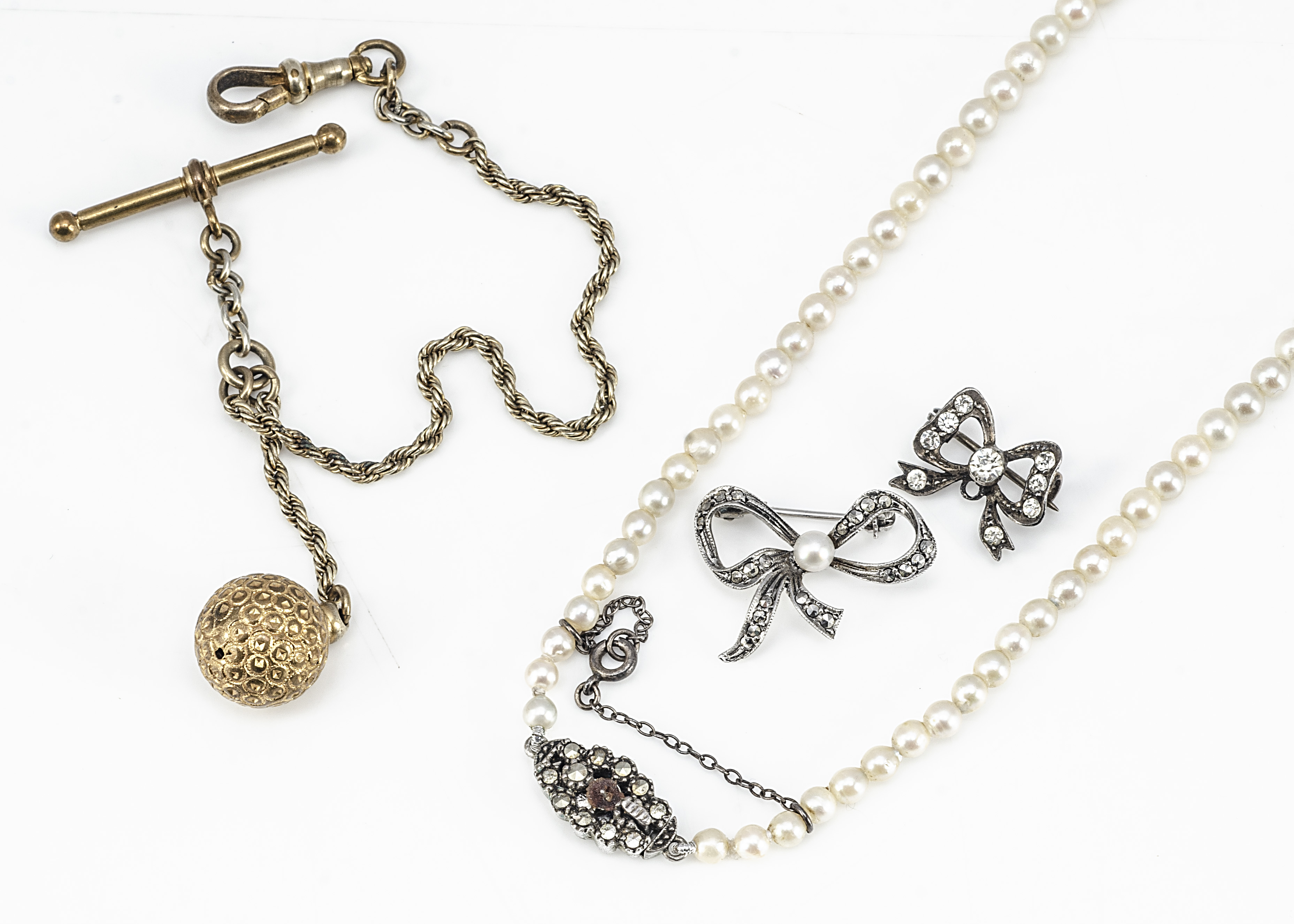 A cultured graduated string of pearls, two paste set bow brooches and a gilt metal fob chain