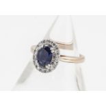 A sapphire and diamond 18ct gold dress ring, the oval mixed cut claw set sapphire surrounded by a