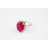 A contemporary white gold ruby and diamond cluster ring, the oval claw set mixed cut ruby surrounded