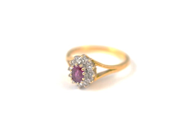An 18ct gold ruby and diamond cluster ring, the oval mixed cut claw set ruby surrounded by a bezel