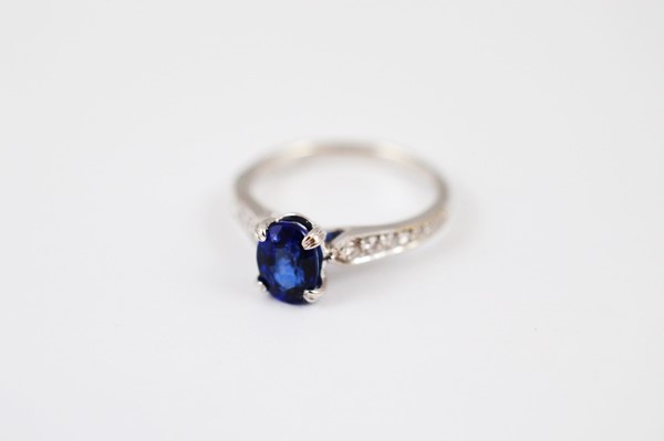 An 18ct white gold sapphire and diamond dress ring, the oval mixed cut claw sapphire in raised