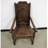 An antique oak arm chair, panelled back with carved initials, scroll arms, shaped frieze with turned