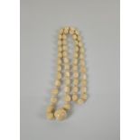 An ivory 'Buddha' bead necklace, with fifty lozenge shaped beads strung with a spherical example,