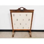 An upholstered fire screen with embroidered floral detailing, surrounded by a carved frame.