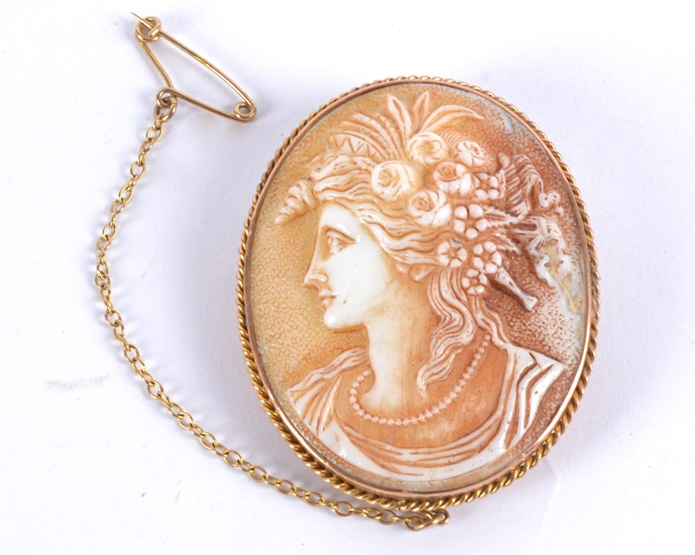 A cameo brooch featuring a woman with flowers in her hair, set in a yellow metal surround,