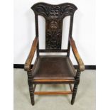 An early 20th Century oak arm / carver chair, shape carved back, face mask to the centre