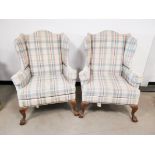 A pair of upholstered wing back arm chairs, raised upon claw and ball feet to the front, later