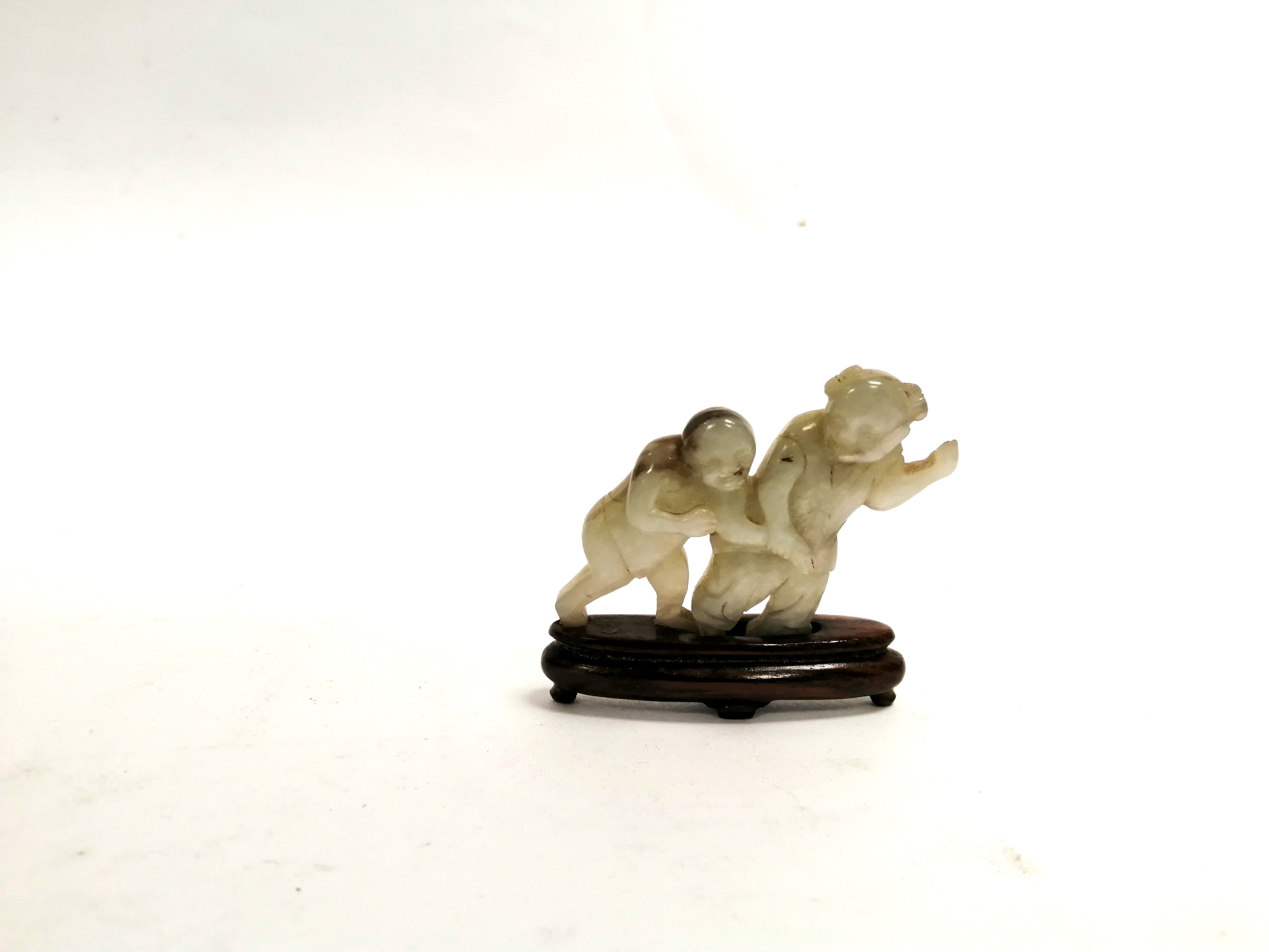 A Chinese hardstone carving of children holding hands, raised on a wooden stand, height 5cm
