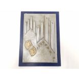 A decorative wall panel 'Sky City', carved and painted piece of wood mounted on a blue board,