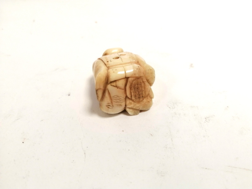 A miniature Japanese ivory okimono of a seated male clasping a creature, with two holes for - Image 4 of 4