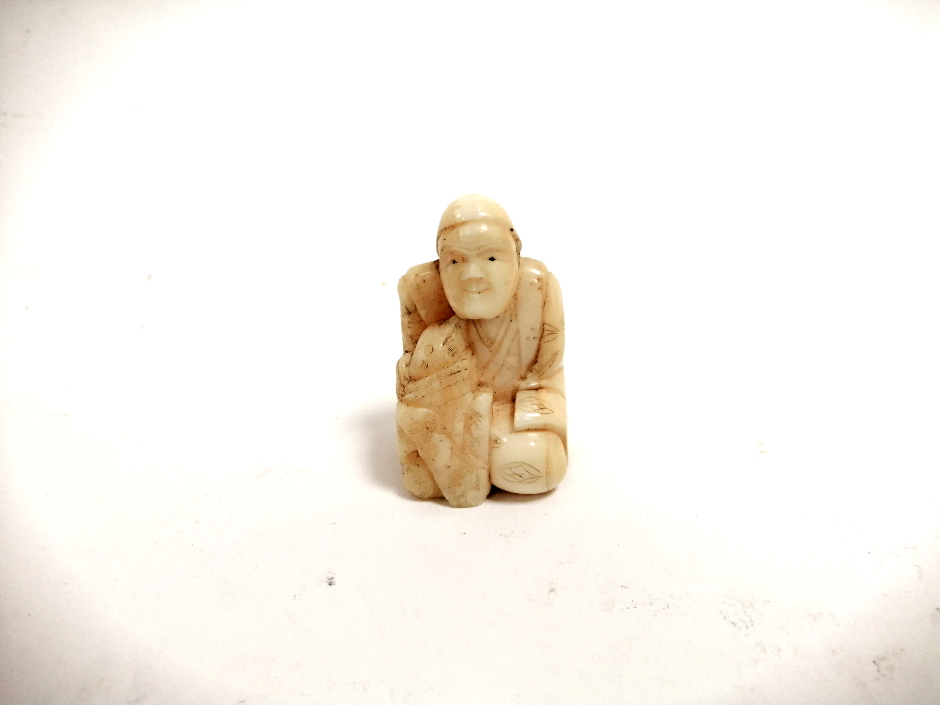 A miniature Japanese ivory okimono of a seated male clasping a creature, with two holes for - Image 2 of 4