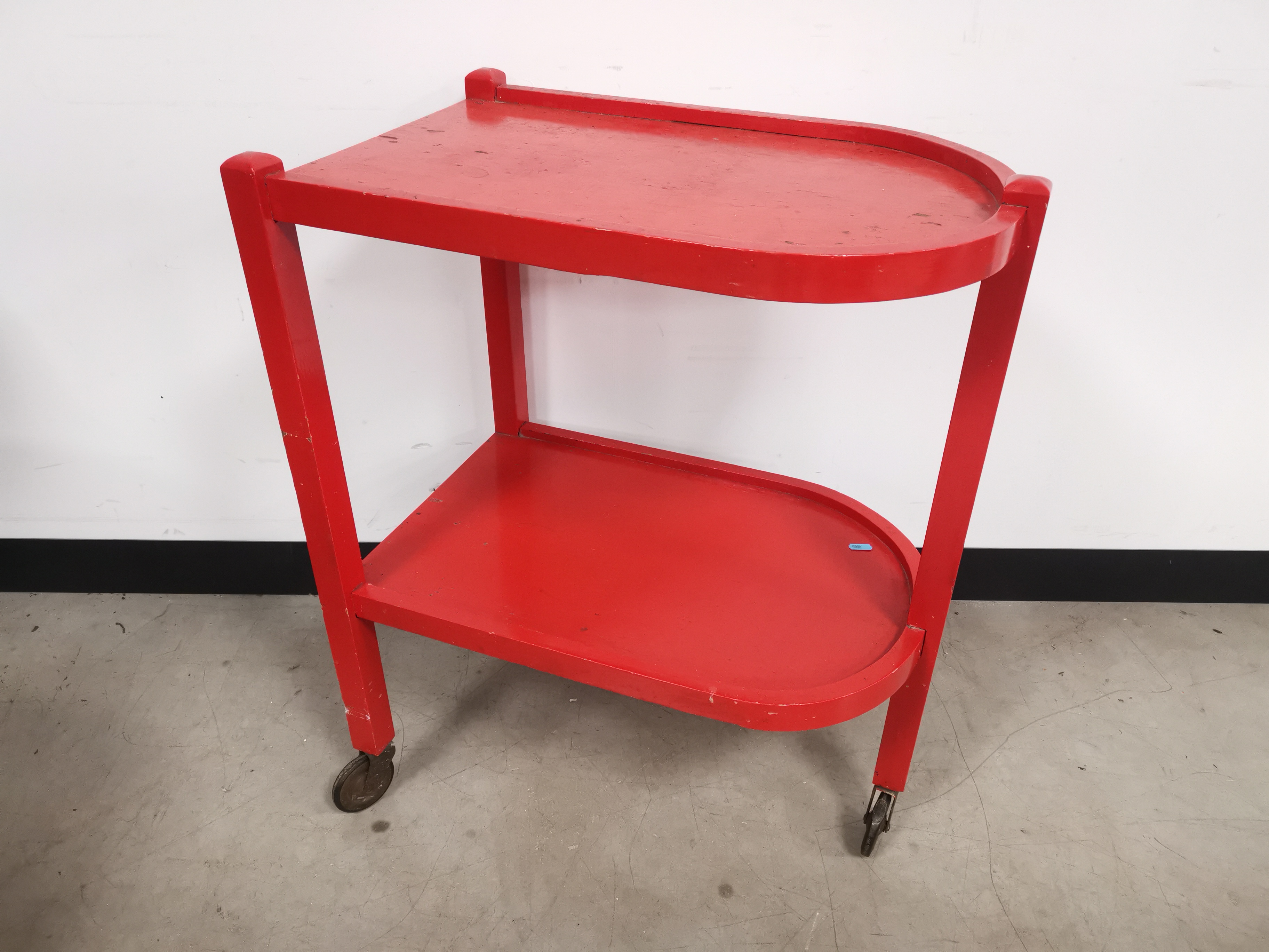 Painted pine two tier trolley, finished in red, raised on three wheels. 60cm W x 41cm D x 77cm H.