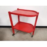 Painted pine two tier trolley, finished in red, raised on three wheels. 60cm W x 41cm D x 77cm H.