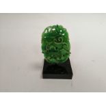 A green hardstone carving of a creature entwined in vines, height of specimen 10cm, raised on a