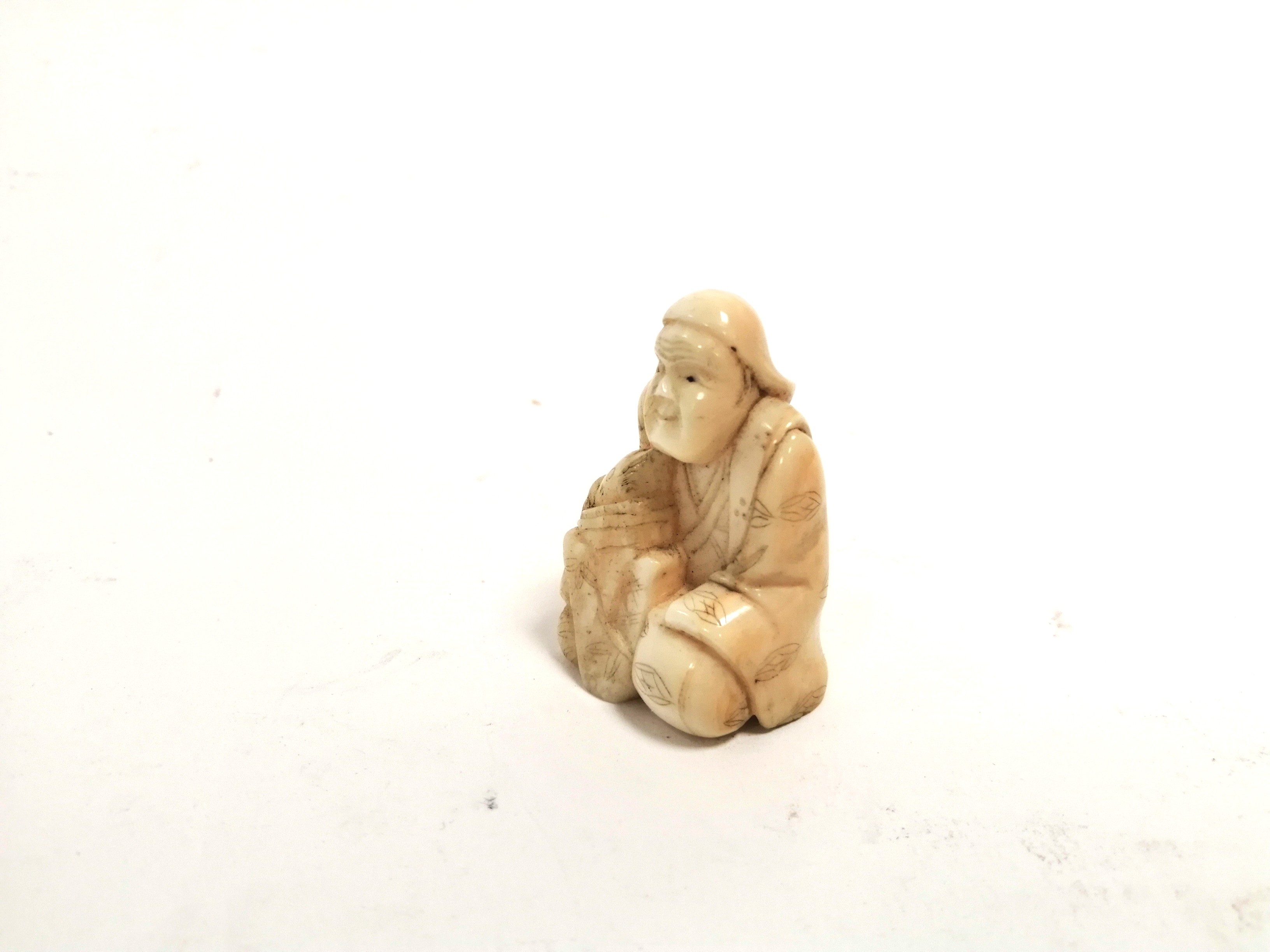 A miniature Japanese ivory okimono of a seated male clasping a creature, with two holes for