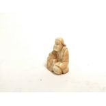 A miniature Japanese ivory okimono of a seated male clasping a creature, with two holes for