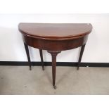 Mahogany demi lune folding tea table, with gate leg raised on cylindrical supports on castors.