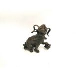 An Asian cast metal figure of a Buddhist lion dog playing with a brocade ball, with curly tail and