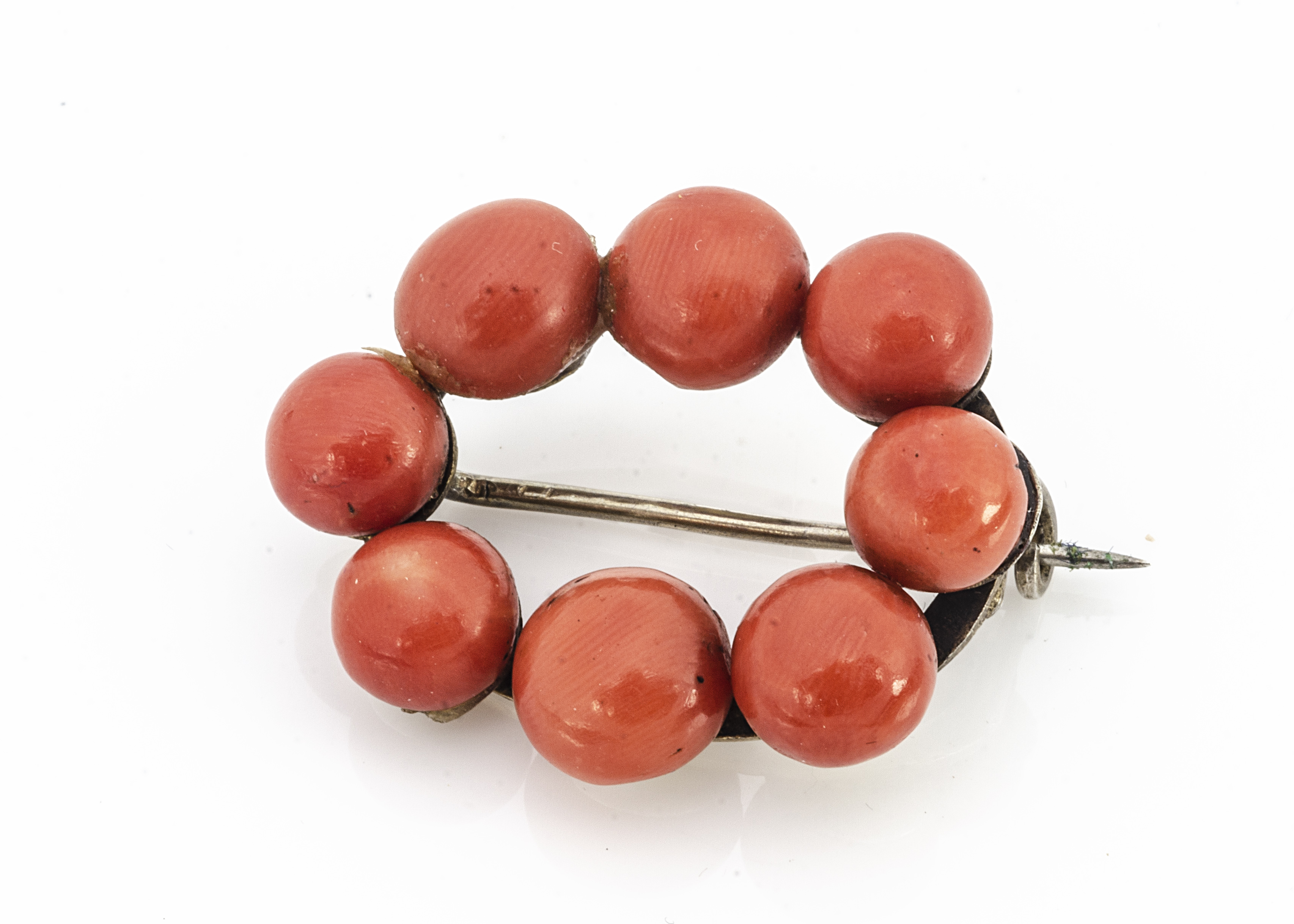 A continental coral and white metal oval bead brooch, the bouton polished coral beads on a white