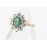 An emerald and diamond cluster ring, the oval mixed cut claw set emerald surrounded by brilliant cut